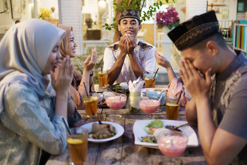Muslim family praying over table with food and drinks